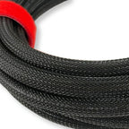 Close-up of a coiled black braided cable with a bright red loop or tie holding it together, photographed on a plain white background.
