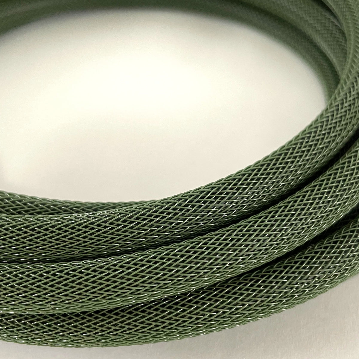 A close-up of a coiled olive green braided cable or cord on a plain light background.