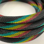 A close-up of a braided black cable or strap with woven diagonal stripes of bright yellow, red, and teal, coiled on a white surface.